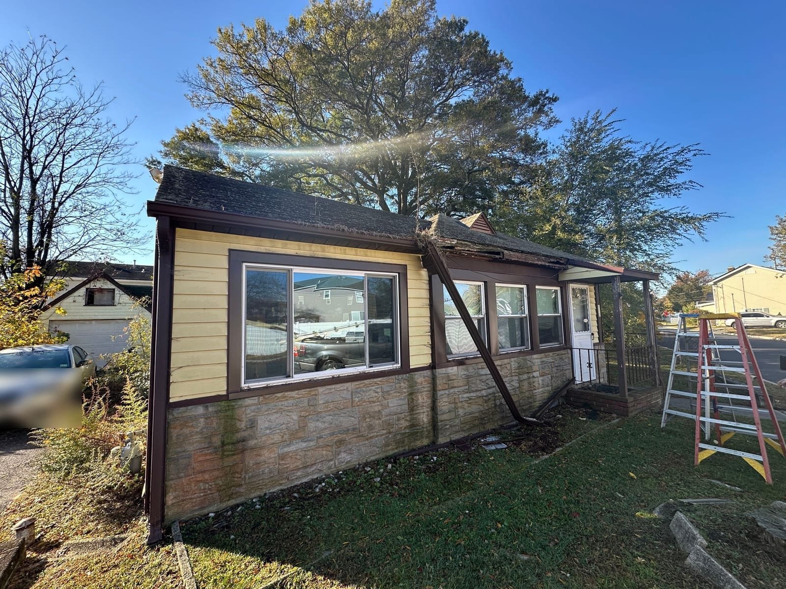 Torn-loose gutter and hanging fascia on porch roofline before repair in Monmouth County NJ
